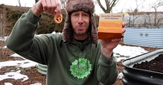 Блогер показує насіння помідорів, вирощених з чізбургера, на фоні зелених рослин.